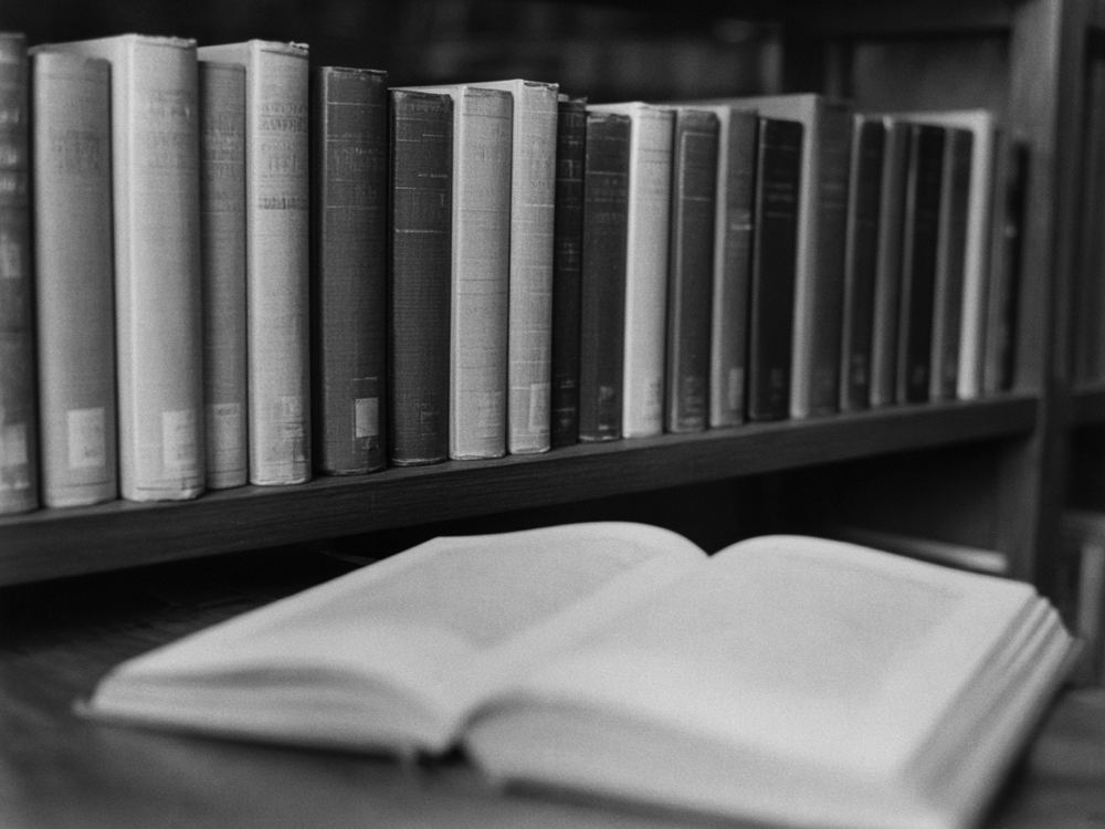 Scholarly books on a library shelf, with an open book in front